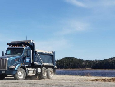 A Maine Department of Transportation dump truck pulls off of the Downeast Sunrise Trail, passing a heap of flotsam deposited by the Machias River. PHOTO: SARAH CRAIGHEAD DEDMON