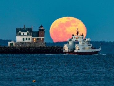 A Maine State Ferry Service boat rounds the Rockland Breakwater as a full moon rises.