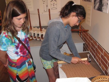 : Maddie Johnson, 11, of Belfast (at left) watches Anna Romano, 11, of Belfast hammer in a rivet in one of the museum’s interactive displays. 