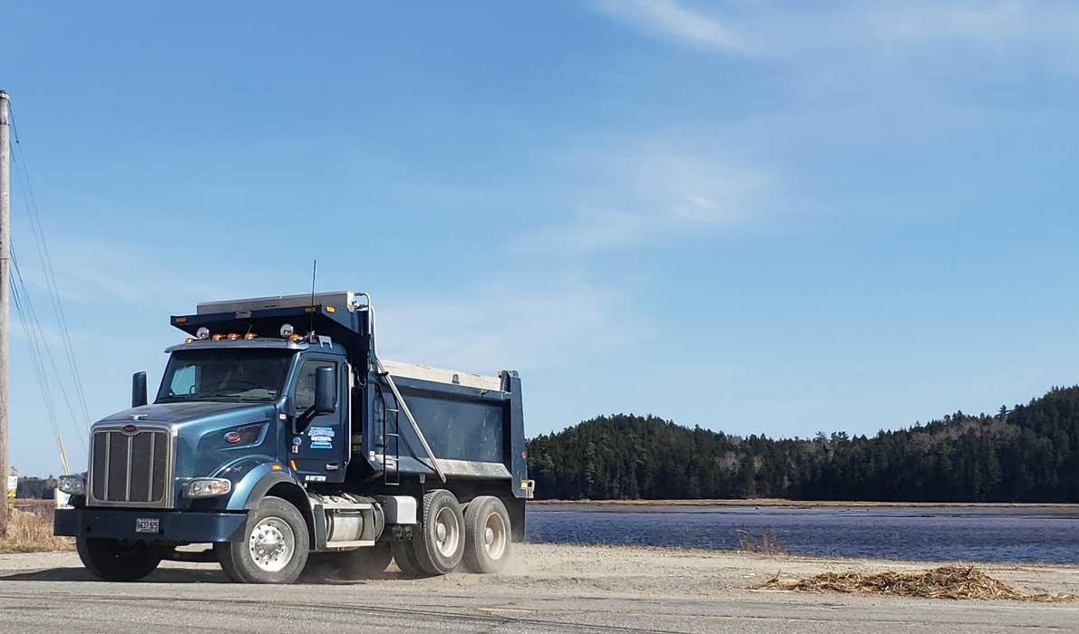 A Maine Department of Transportation dump truck pulls off of the Downeast Sunrise Trail, passing a heap of flotsam deposited by the Machias River. PHOTO: SARAH CRAIGHEAD DEDMON