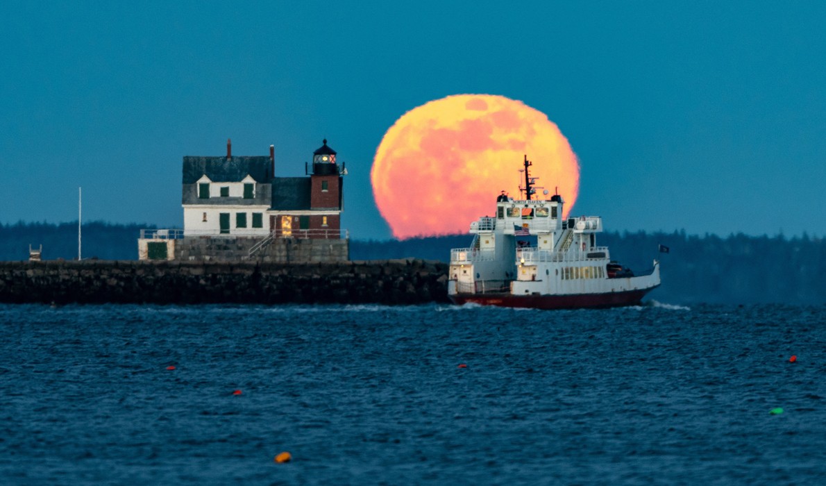 A Maine State Ferry Service boat rounds the Rockland Breakwater as a full moon rises.